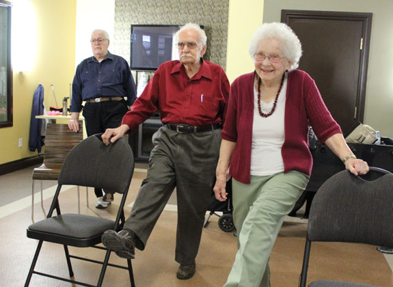 A smiling older couple performs standing exercises together