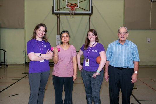 Two young women and two older adults smiling and standing in a gym