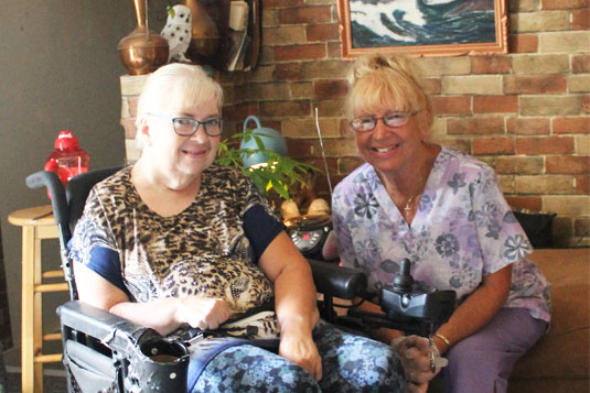 Two smiling woman in a home; one is in a wheelchair
