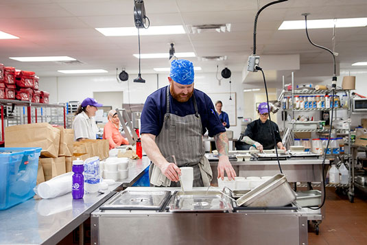 A bearded man serving food in a professional kitchen