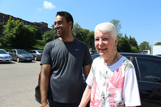 A smiling young man and a smiling older woman in front of a car