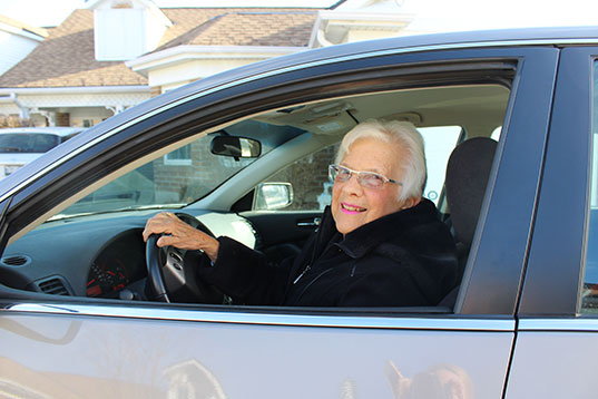 A smiling older woman driving a car