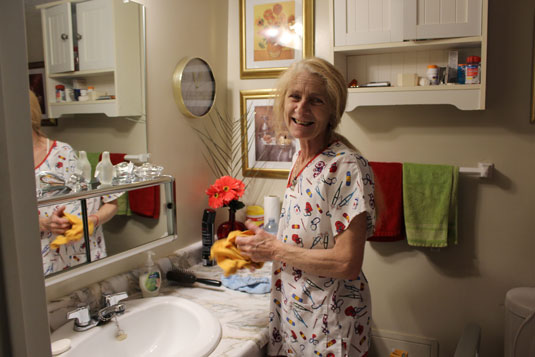 A smiling older woman cleaning a bathroom sink