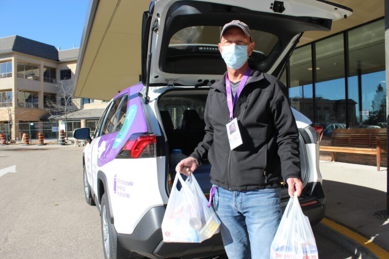 A volunteer delivering groceries from their car's trunk